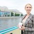 Happy woman with drink standing by riverside during travel on steamer